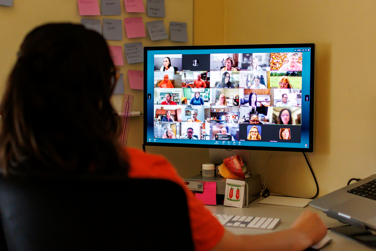 A person looking at a computer screen during a video conference with multiple participants displayed in individual windows.