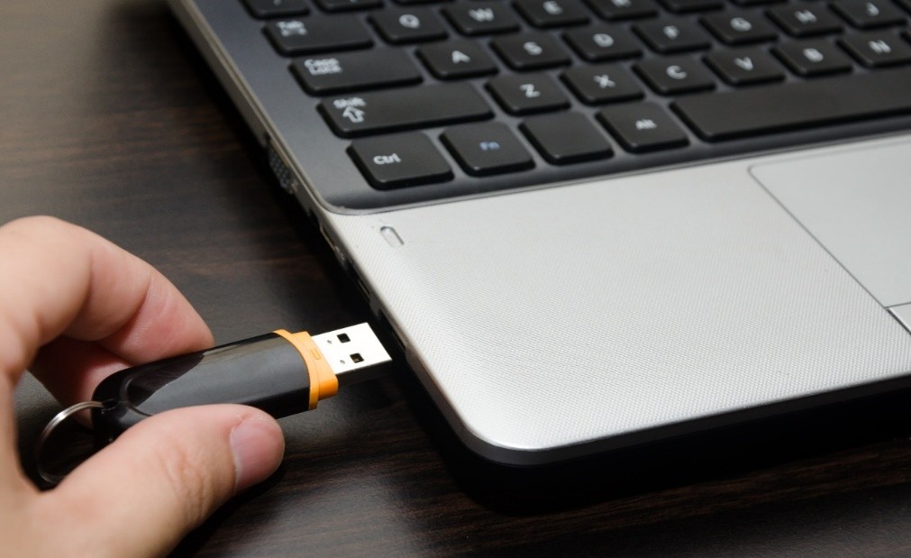 A person plugging in a black USB drive into a laptop.