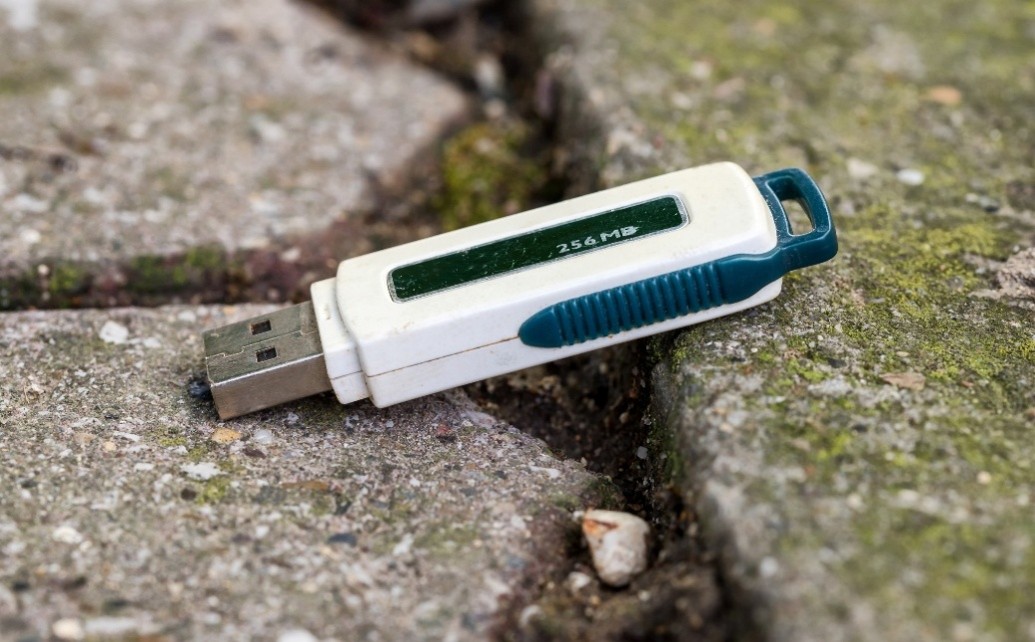 A white USB drive sitting on the ground in between concrete.