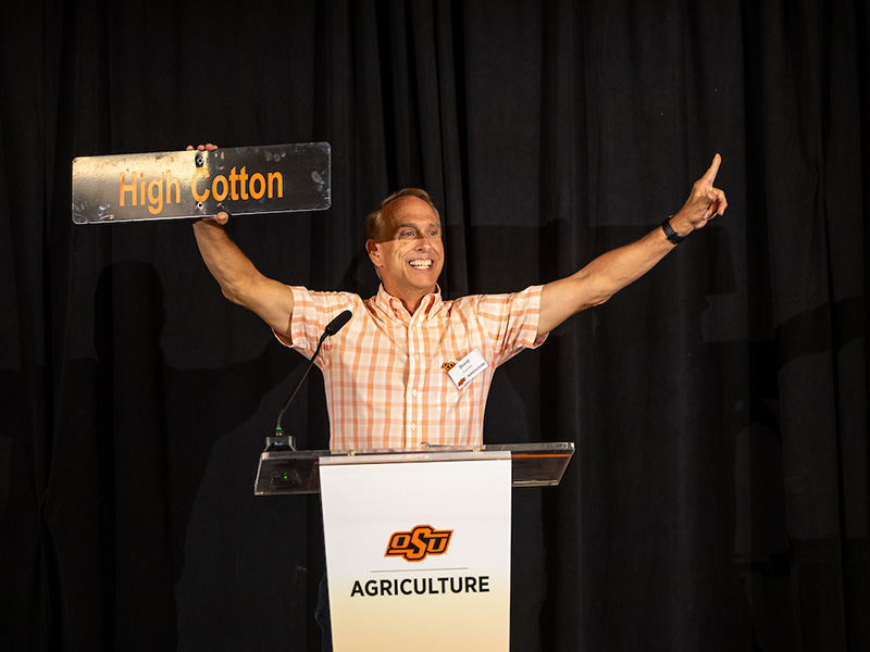 A man standing at a podium giving double finger guns while smiling.