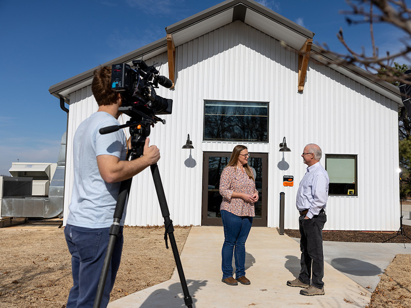 Two people being interviewed for a television show while beiing filmed with a large camera.