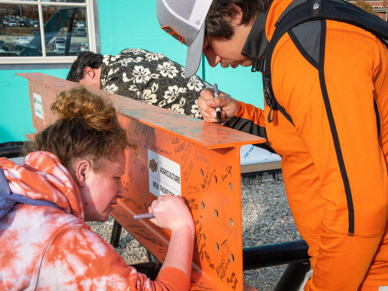 People signing an orange construction beam