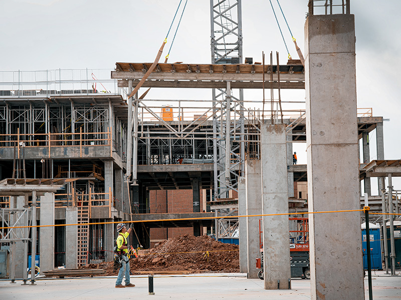 A person on a construction site guiding a crane setting forms for second floor of a building. 